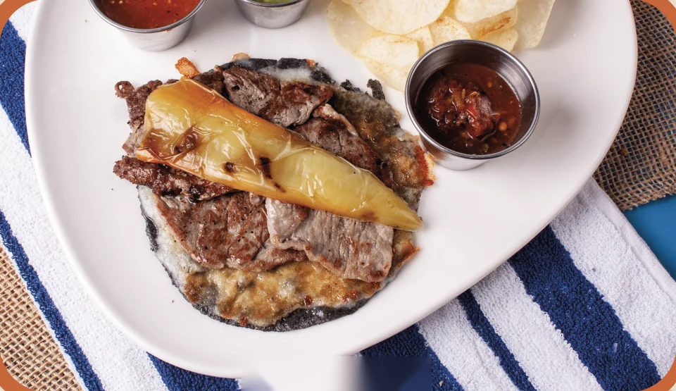 Gaonera de ribeye con costra de queso y chile asado, acompañada de salsas taqueras